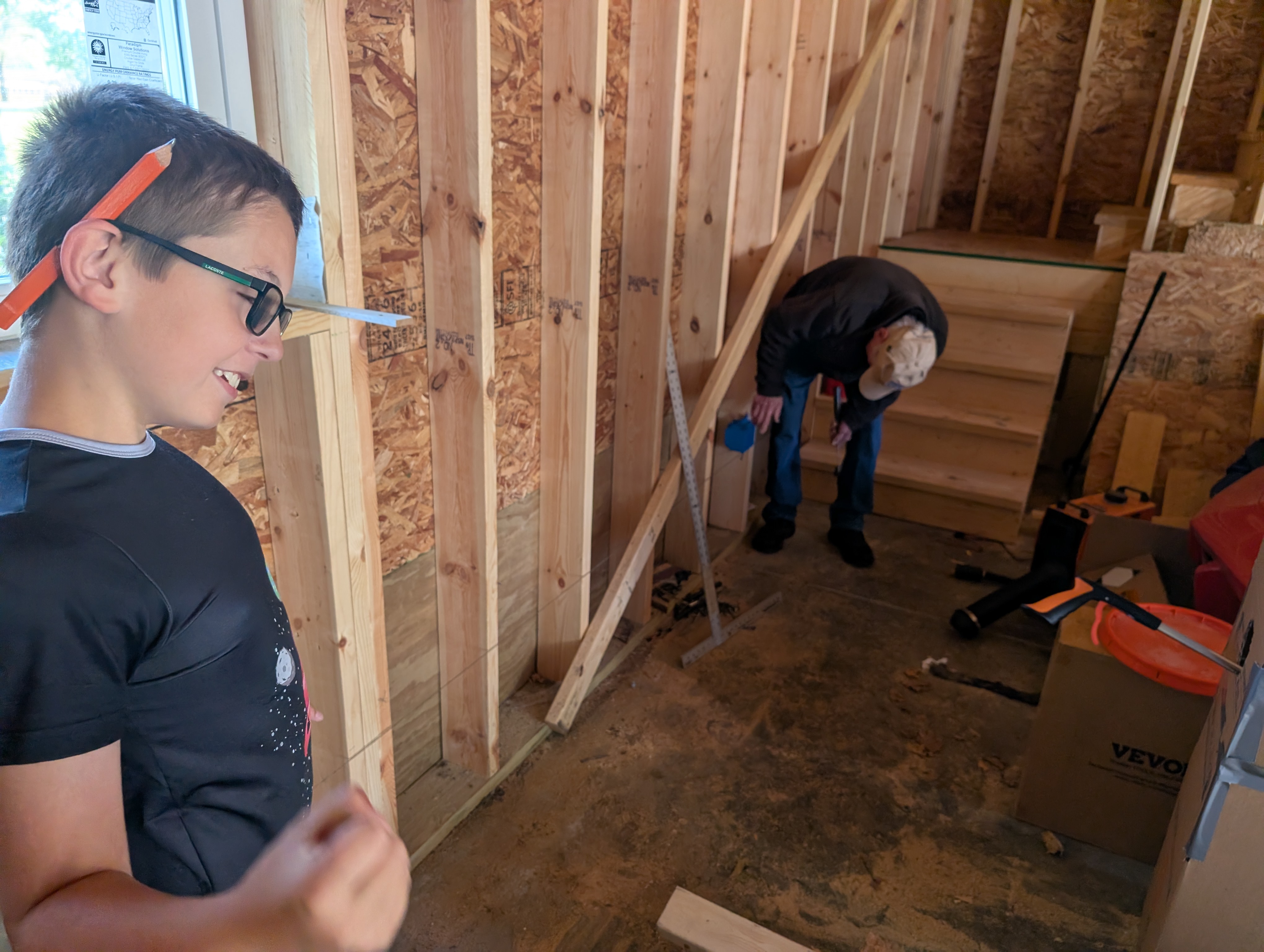 Conor with pencil behind ear; Uncle Ed bent over at the bottom of the stairs working on tools