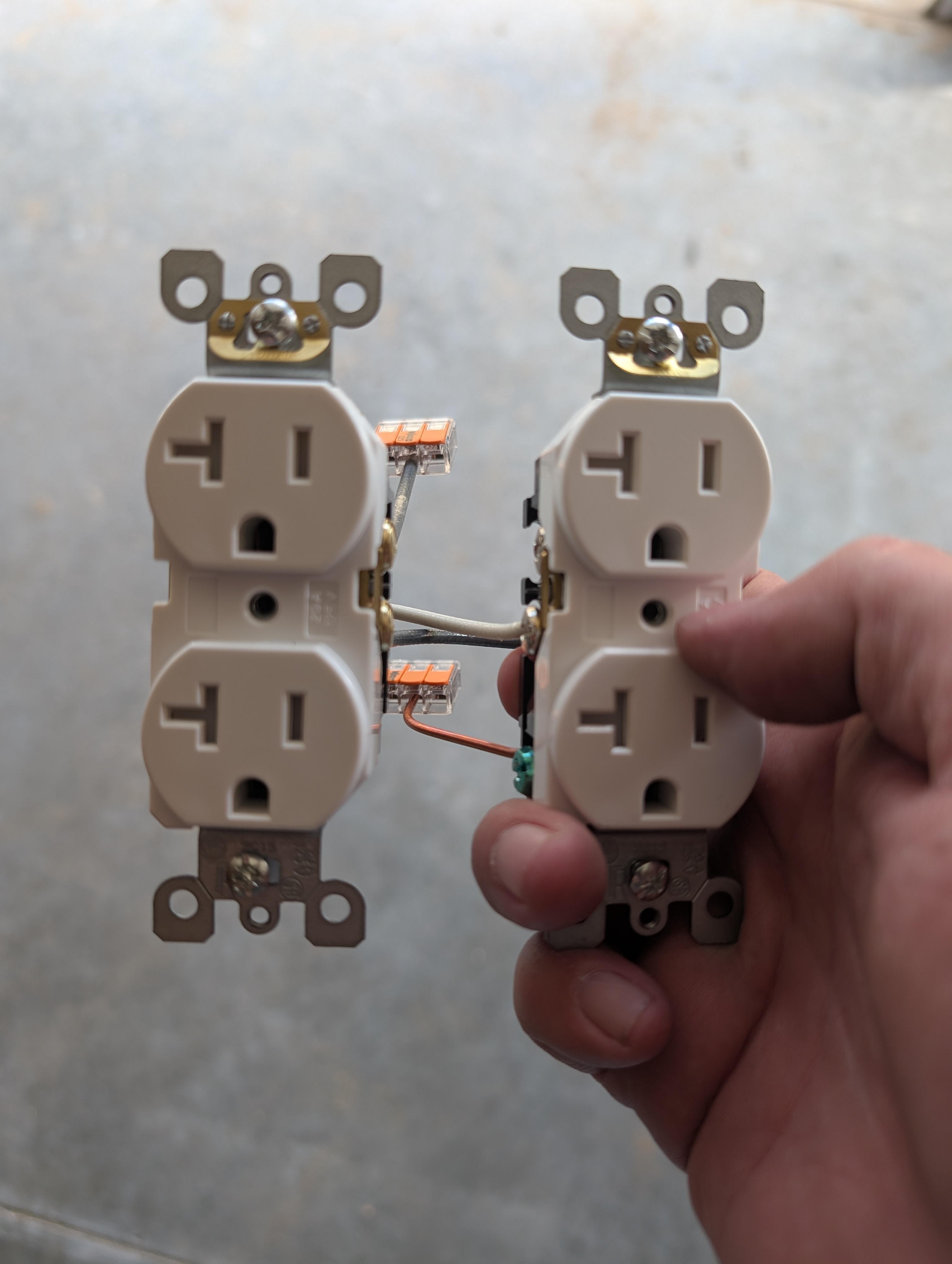 Two 20A duplex outlets held side-by-side, wired together with WAGO 221 lever-nuts on each conductor — neutral, hot, and ground bridged between the two devices