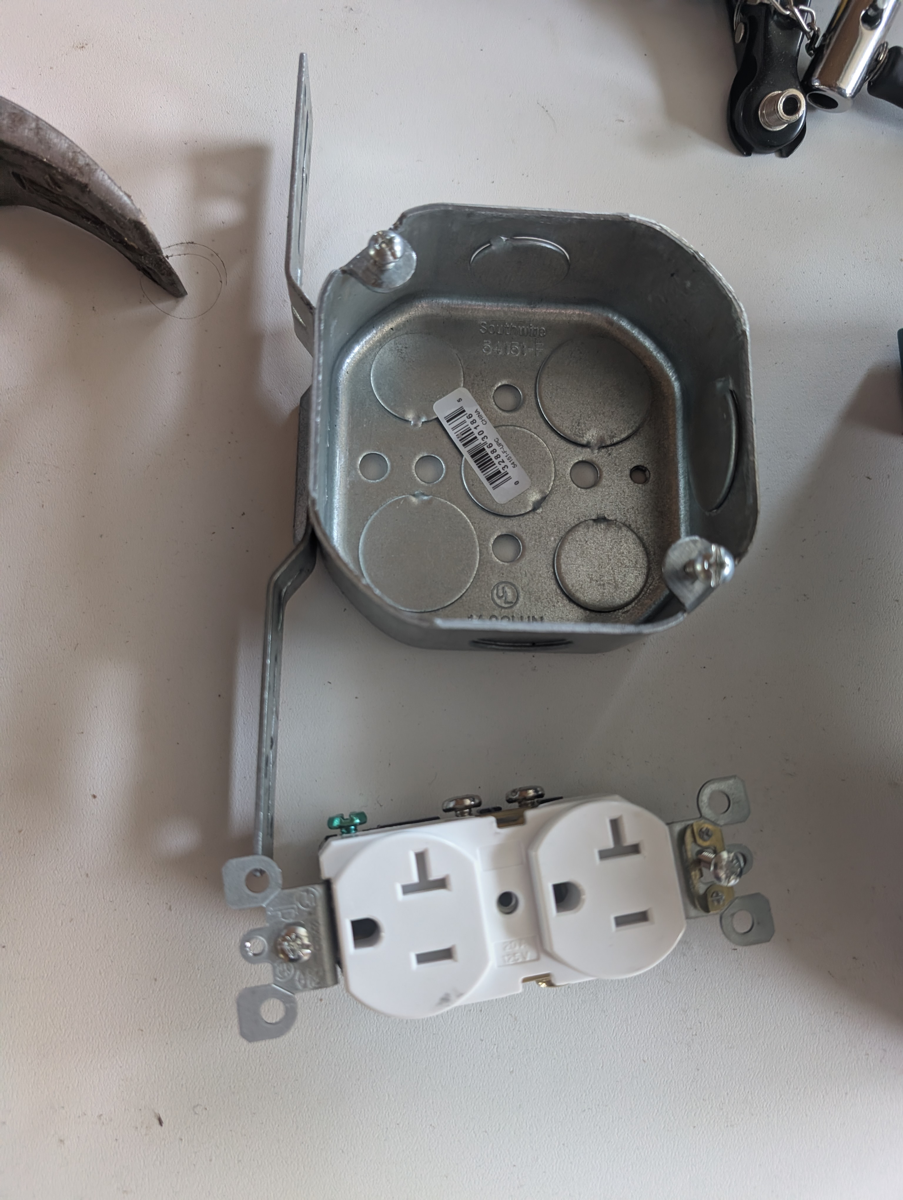 Southwire 4 inch octagon box with F-bracket above a 20A duplex receptacle, showing the device-yoke screws do not align with the box