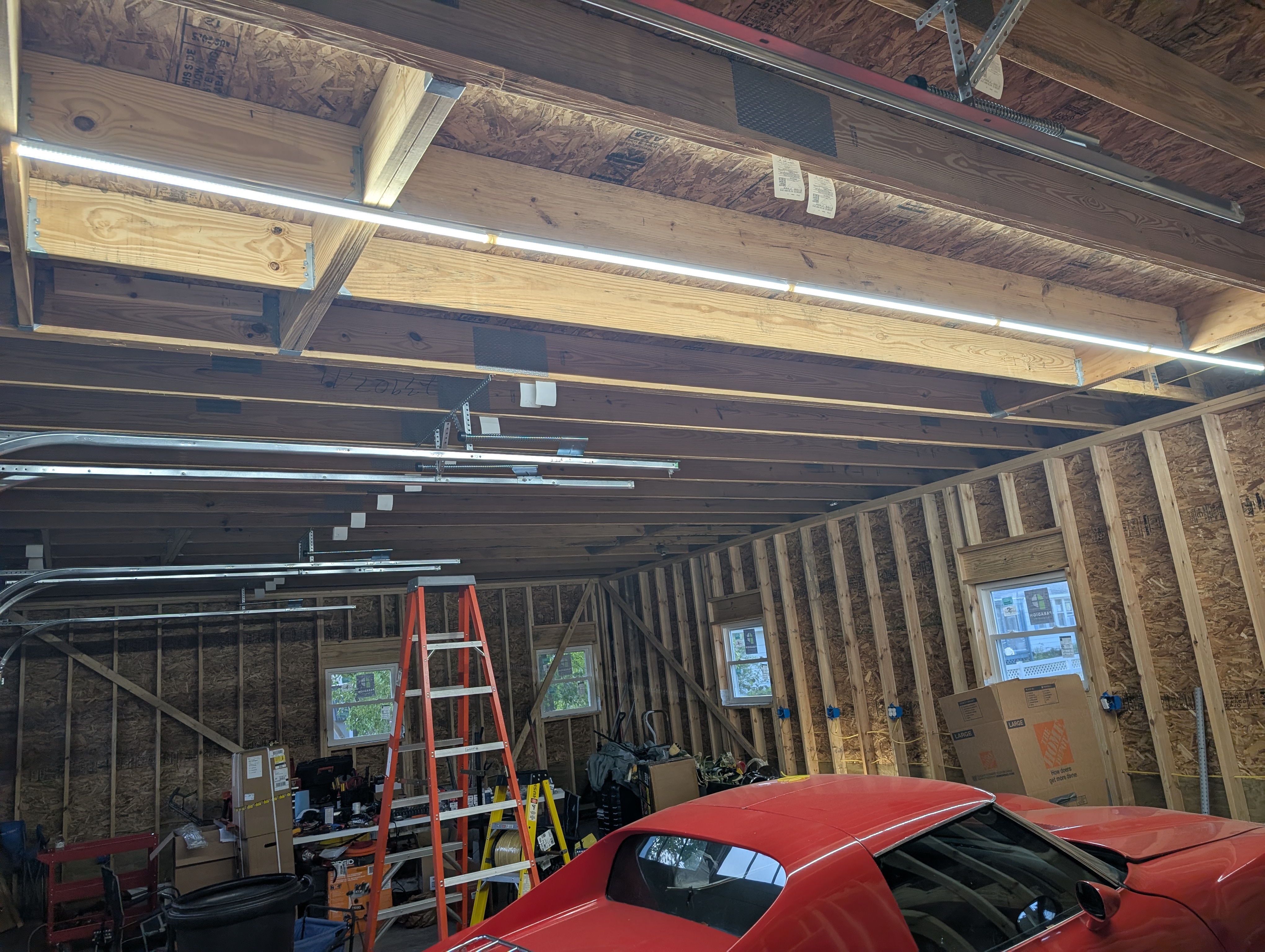 Wider interior view of the lit five-fixture LED run along the garage ceiling, with a red car parked in the bay below and the loft stairs at left