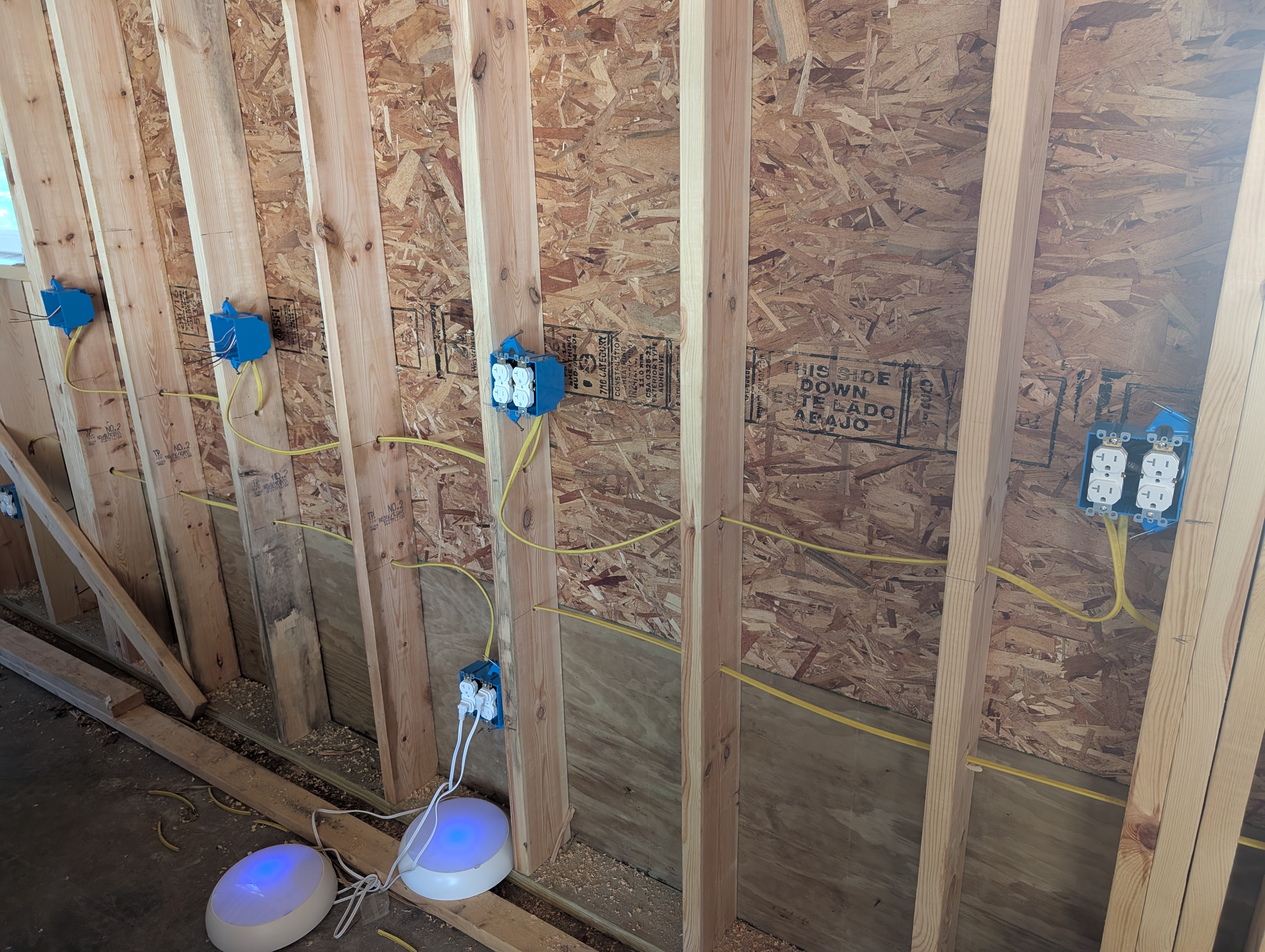 North wall framing with two workbench-height duplex receptacles installed and the remaining boxes still empty