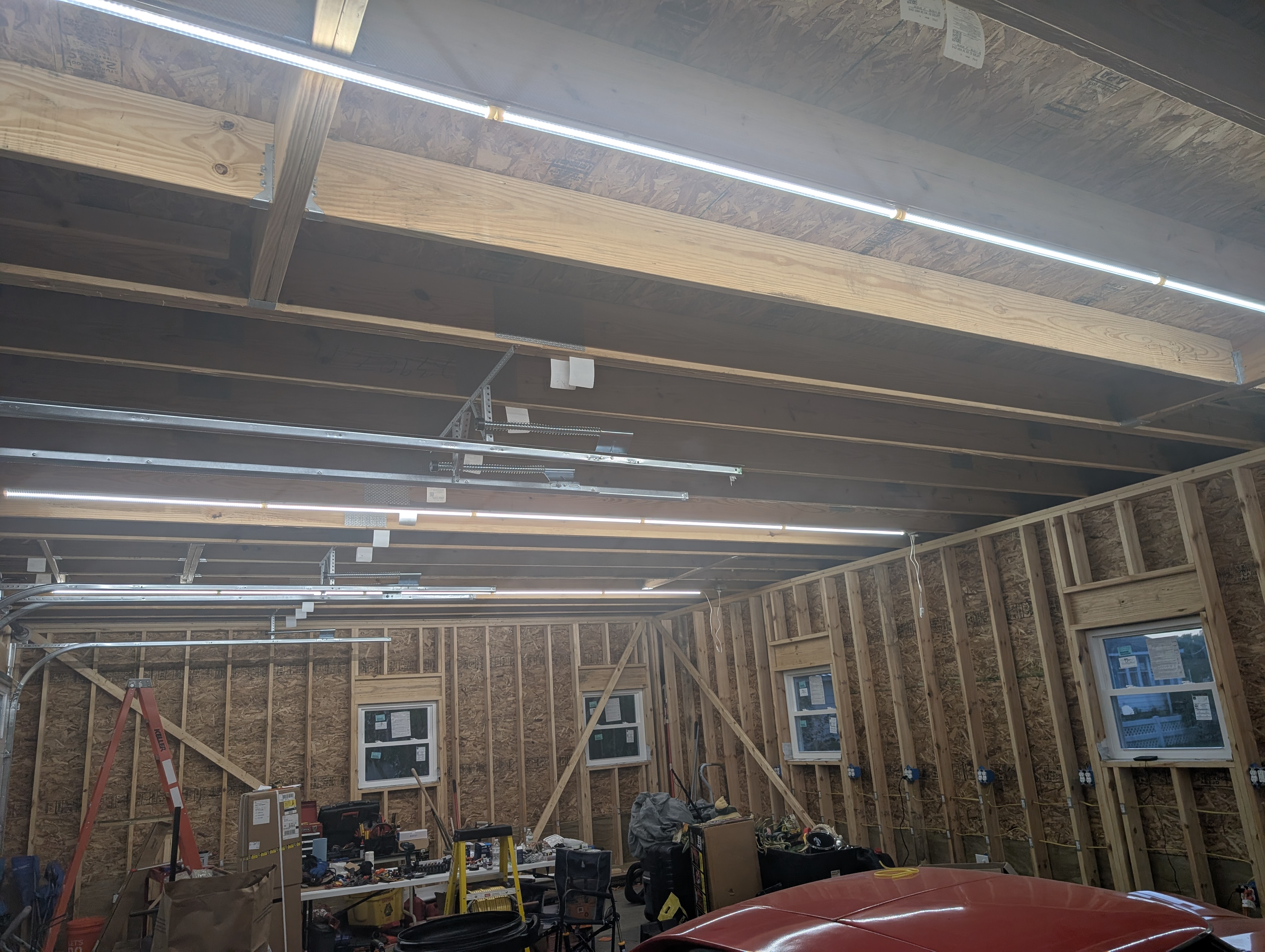 Looking up at the loft-floor trusses with three rows of Barrina LED shop lights lit, brightly illuminating the garage at night
