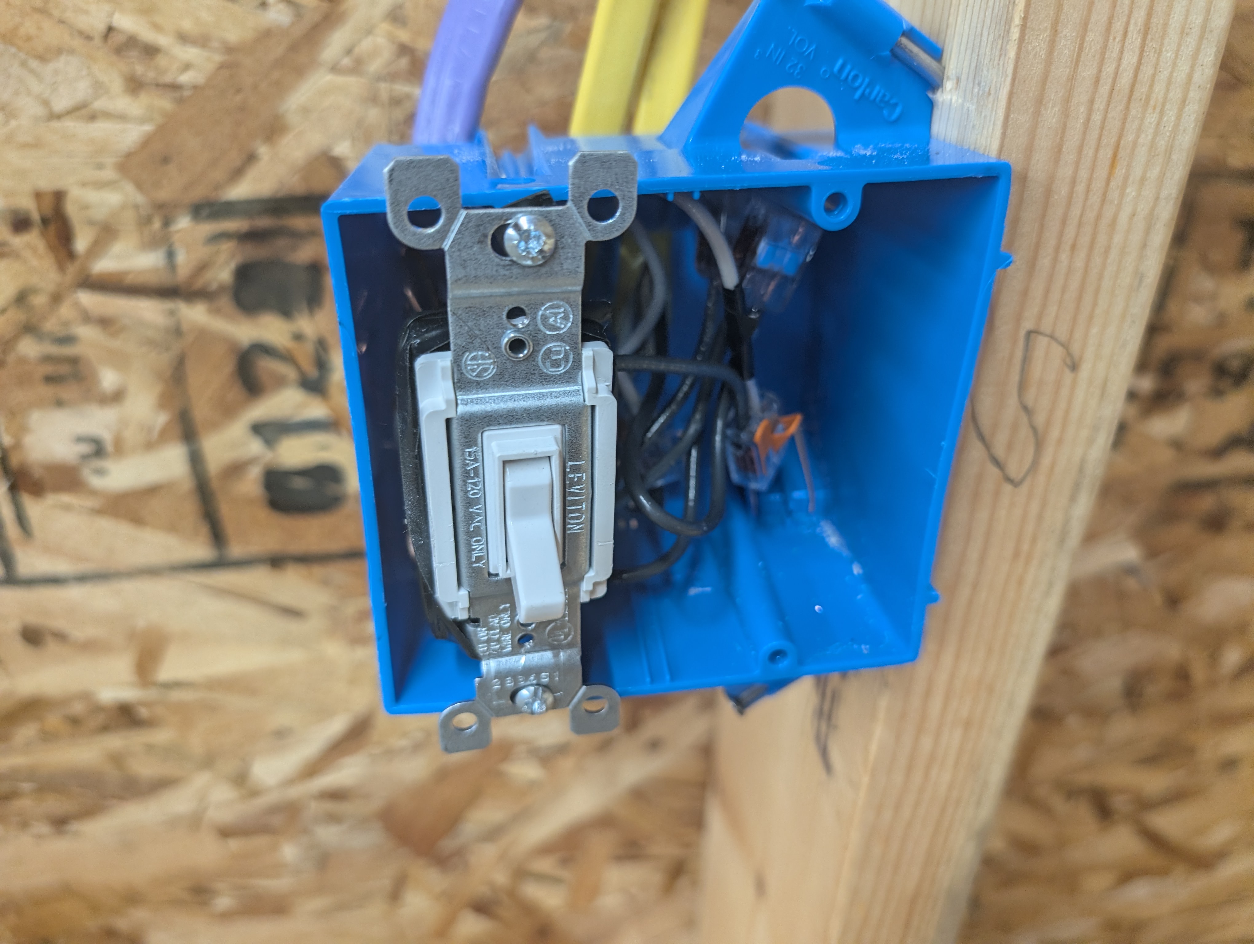 Open 2-gang blue switch box at the stairwell with the garage-floor-light 3-way toggle installed on the left gang, showing the two 12/2 cables, one 12/3, and Wago lever-nut splices in the back