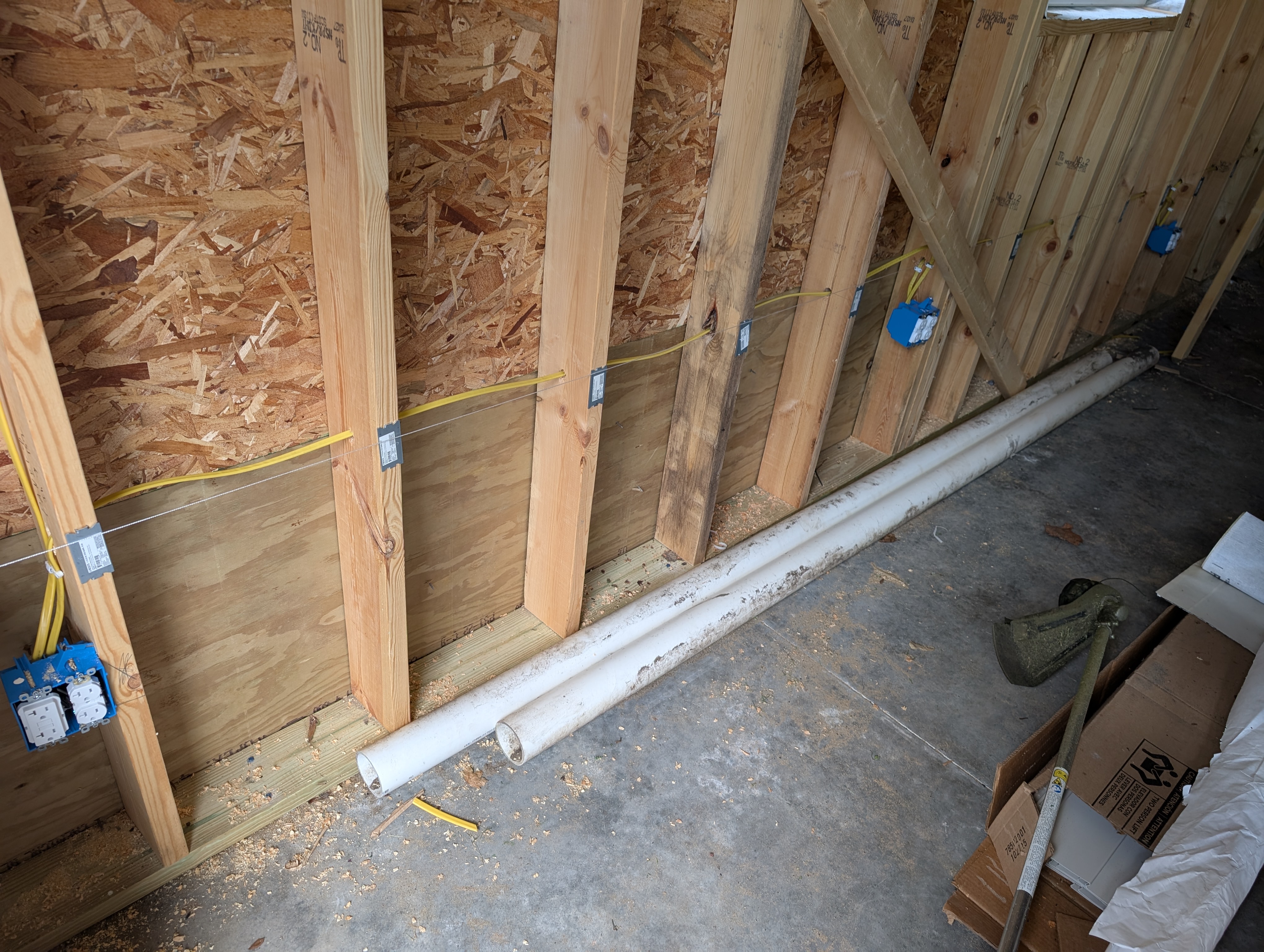 Closer, head-on view of the west wall showing the horizontal NM-B run across the studs with steel nail plates protecting the cable, and the dual-gang GFCI box at left