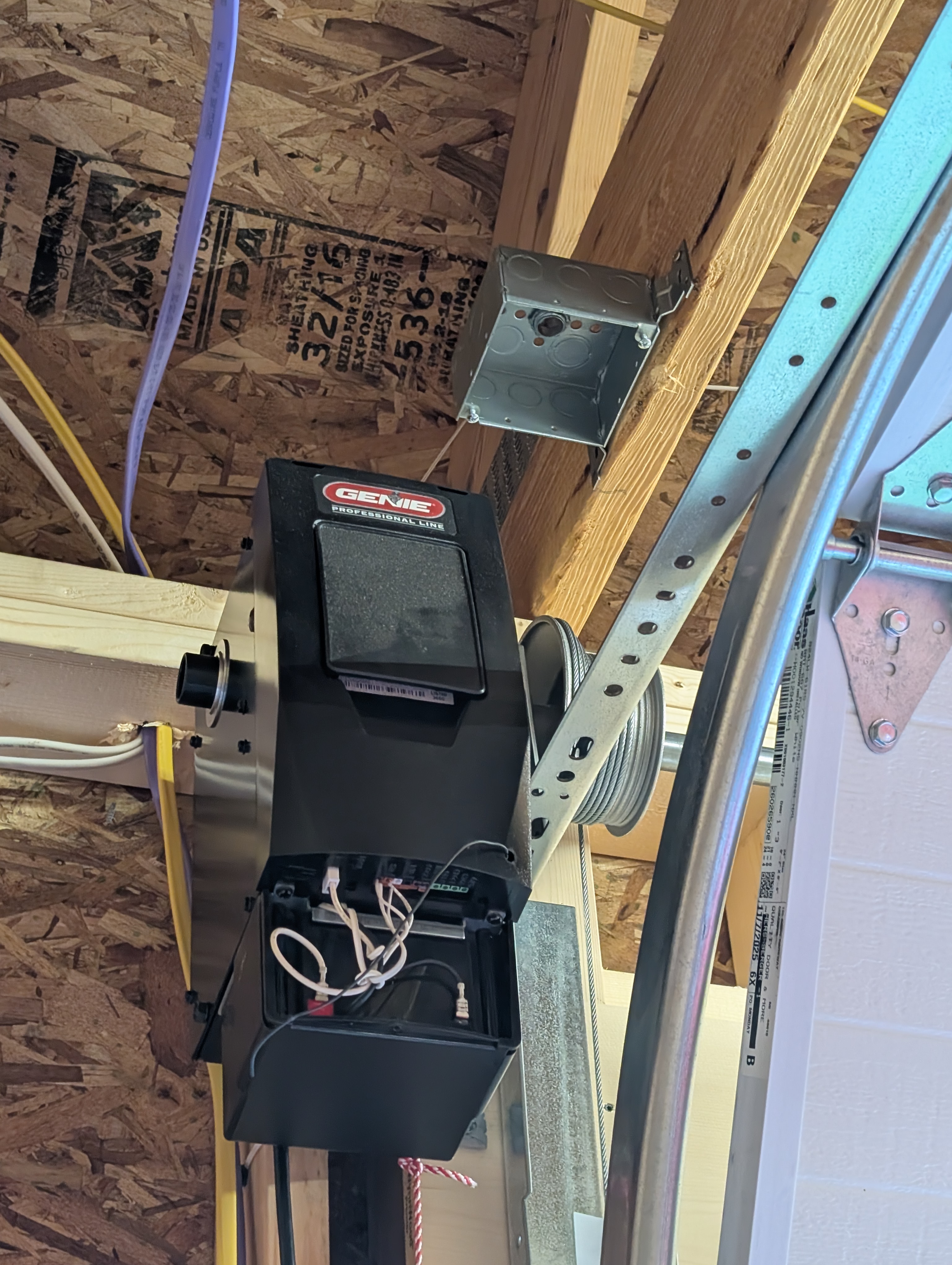 Genie Professional Line garage-door opener head with a metal ceiling box mounted on the framing just above/beside it; opener rail and counterbalance hardware visible