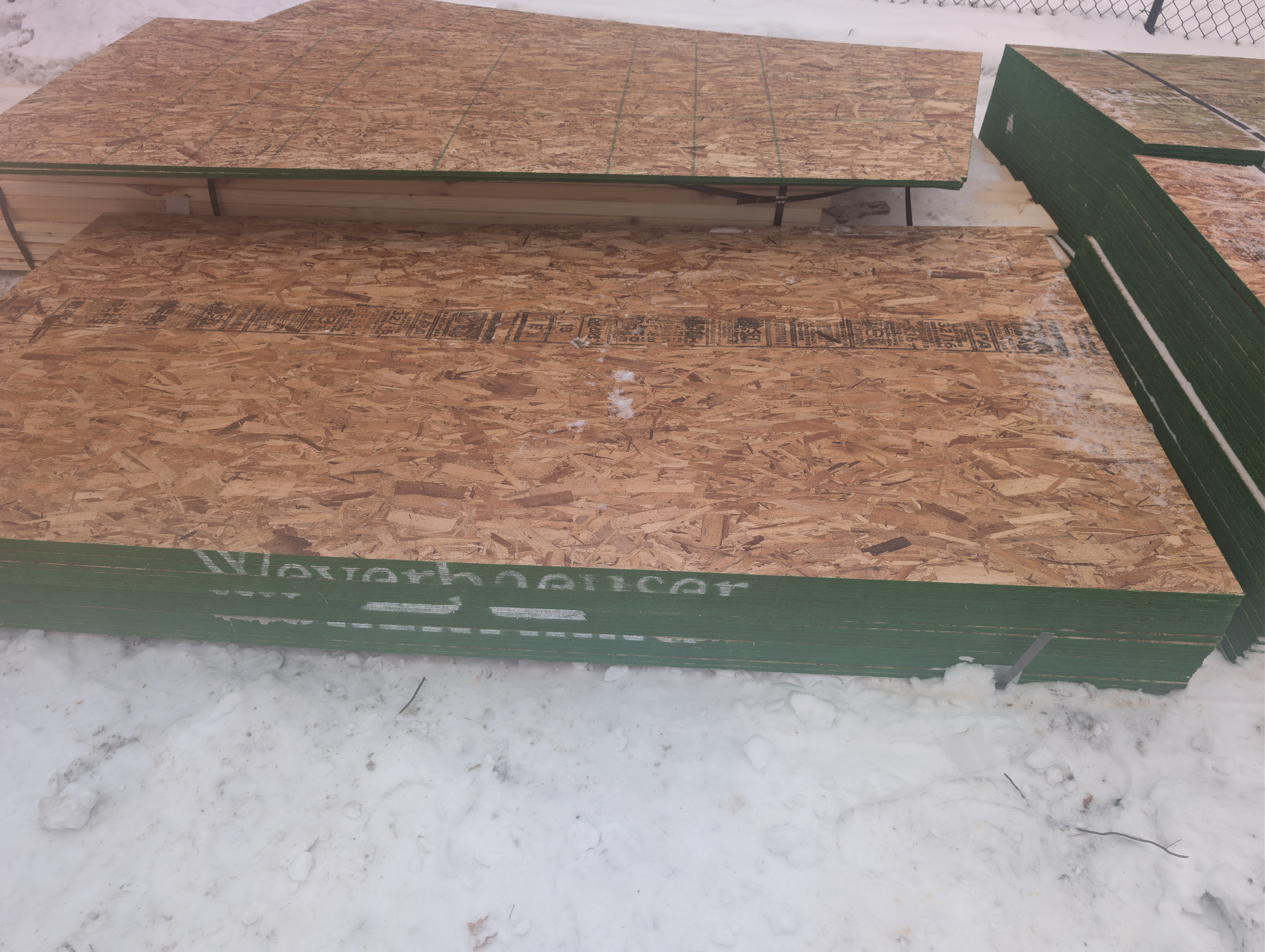 Stacks of green-edge OSB panels staged on site