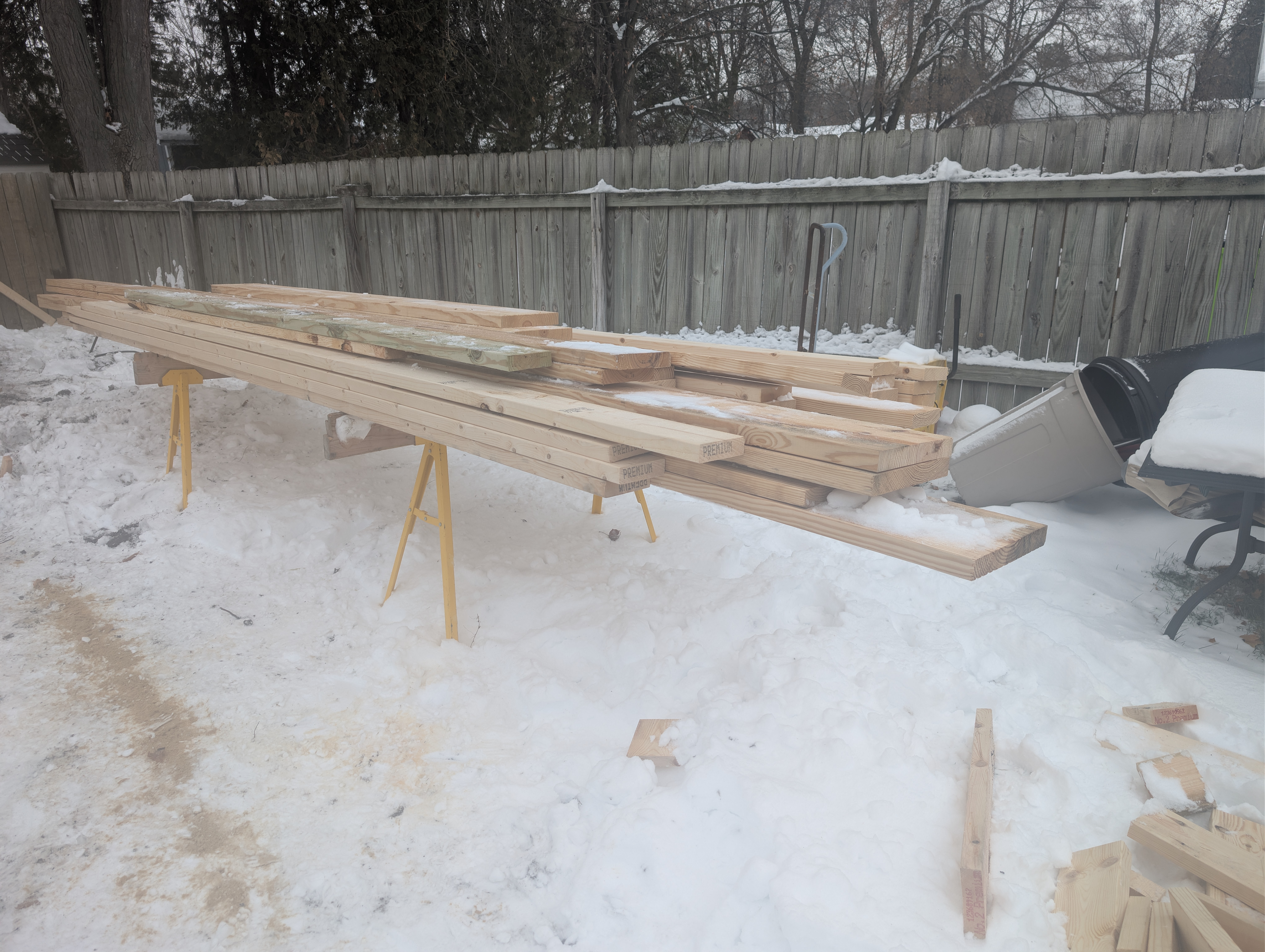 Dimensional lumber staged on sawhorses beside fence