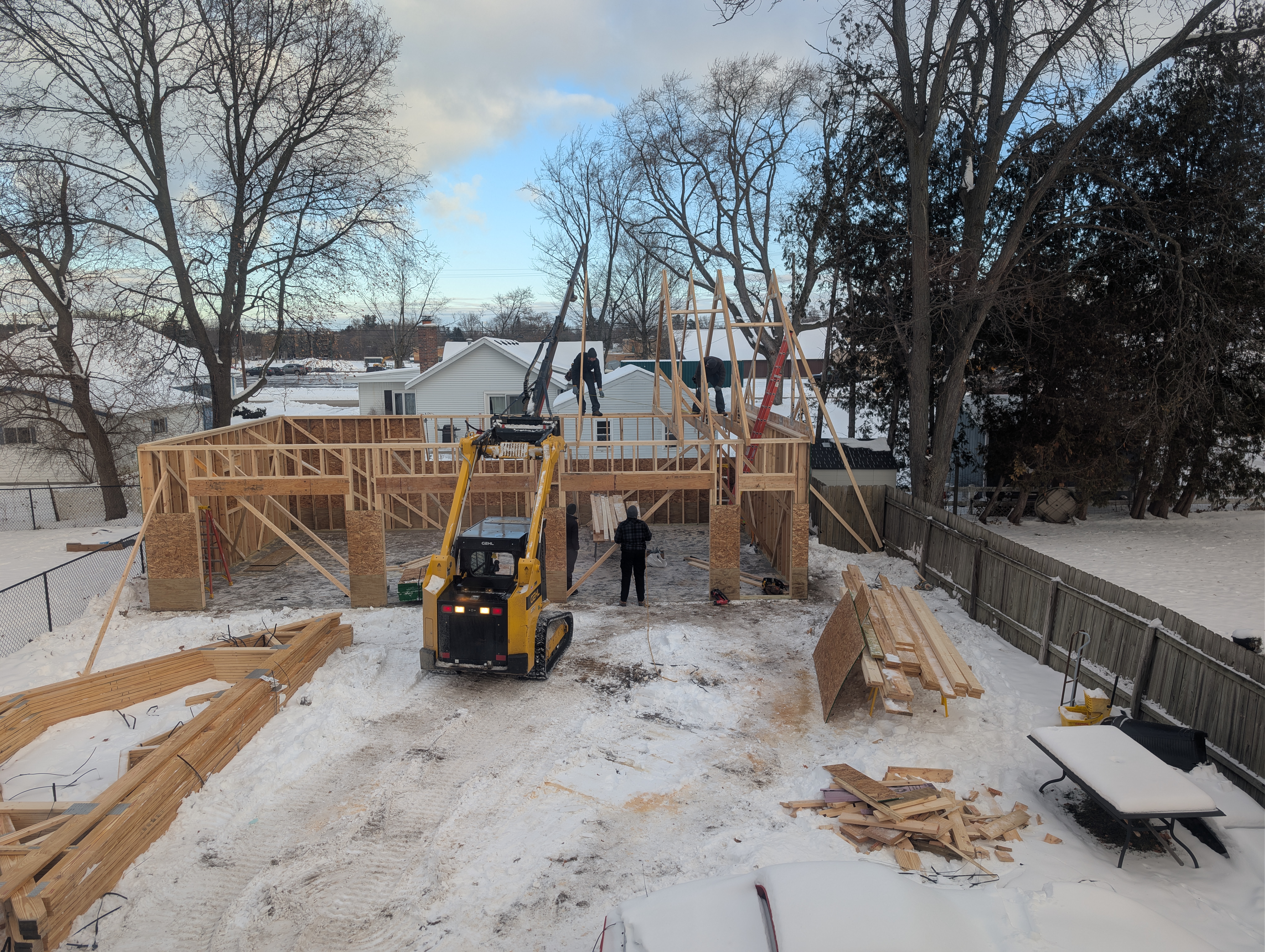 Loader lifting roof trusses while crew braces walls