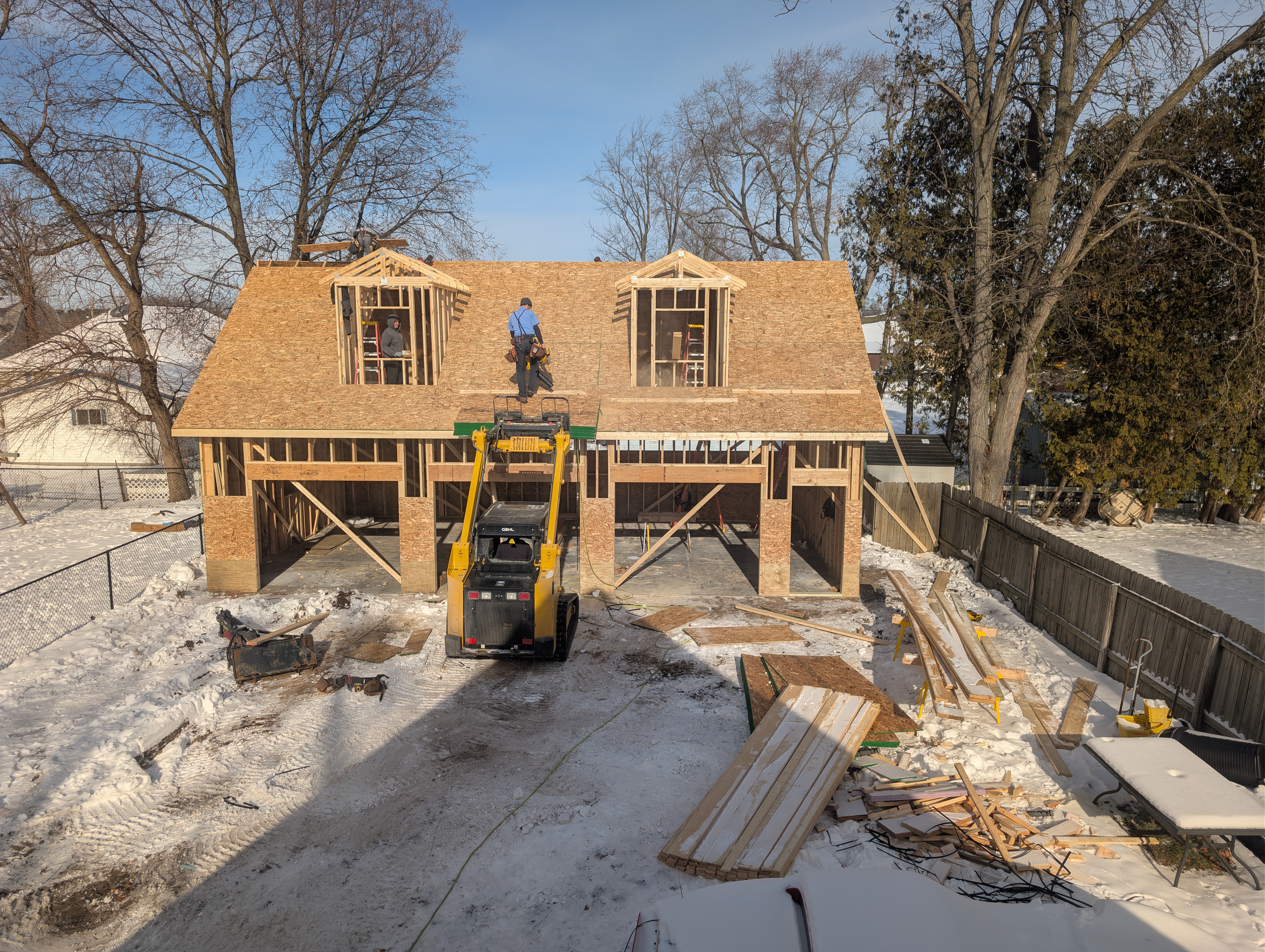 Crew lifting roof sheathing to dormers with skid steer