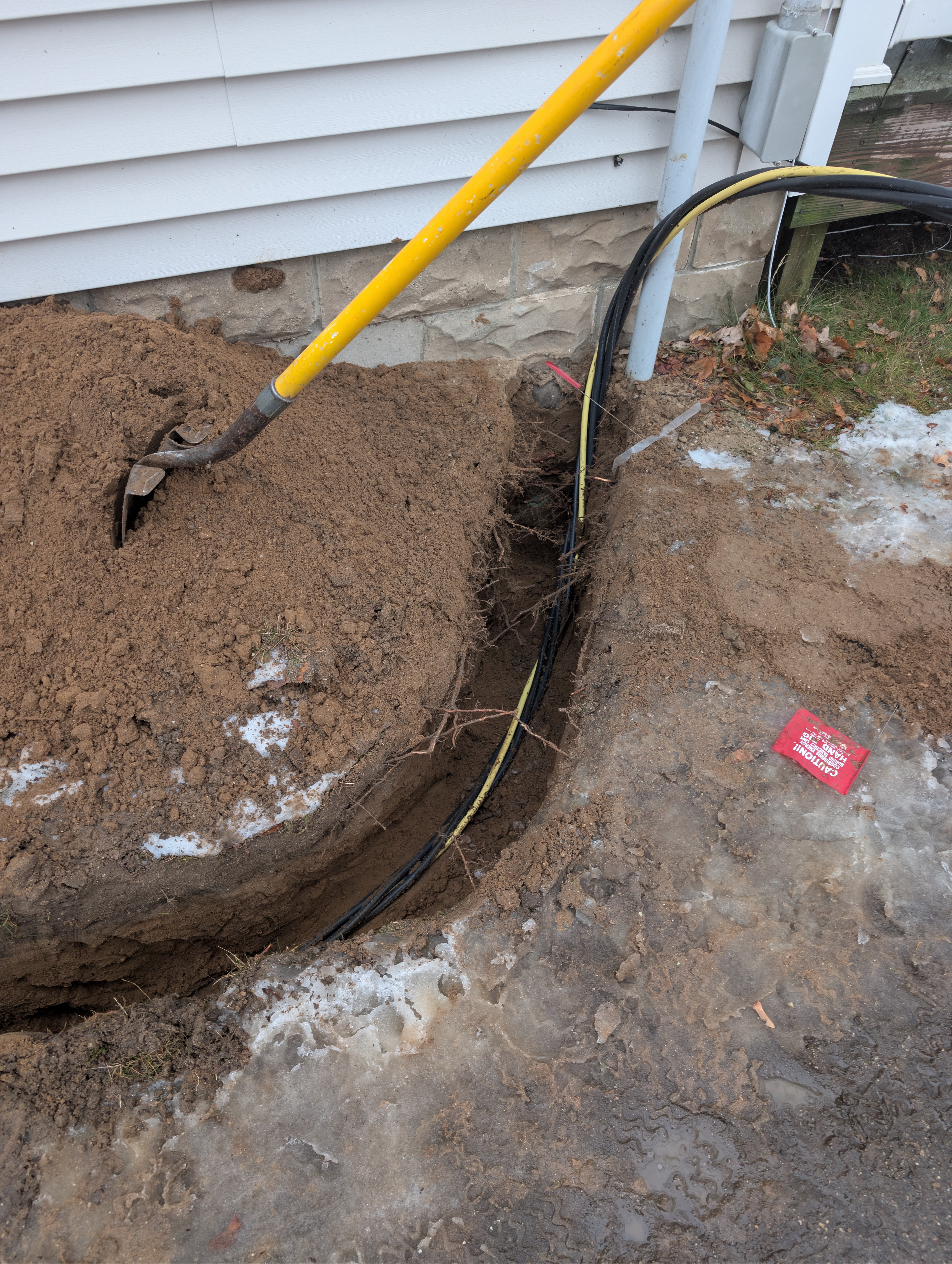 Close-up of electrical trench at house foundation with wire entering ground