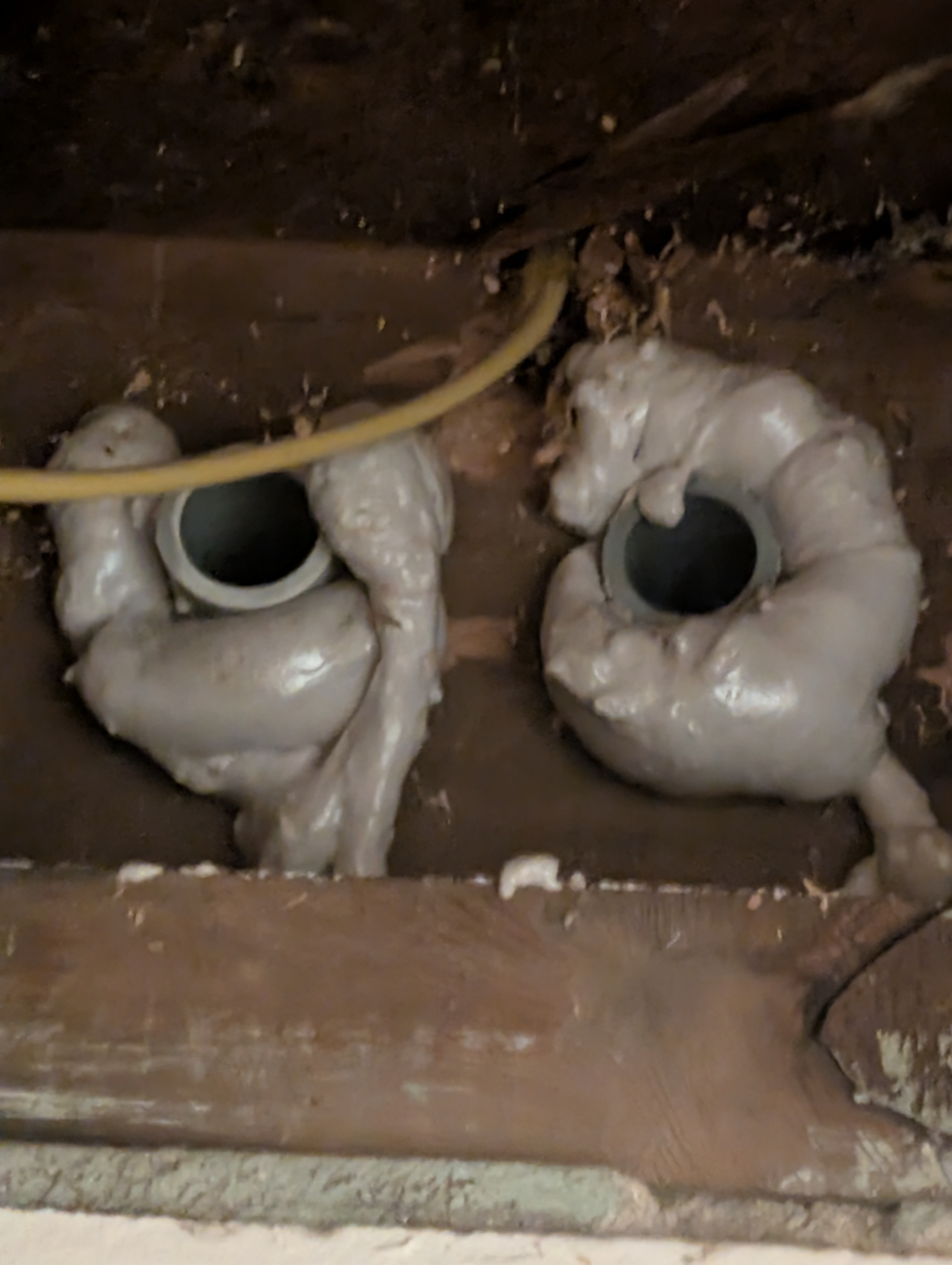 Wide angle view of two foamed-in conduit penetrations through house basement block wall